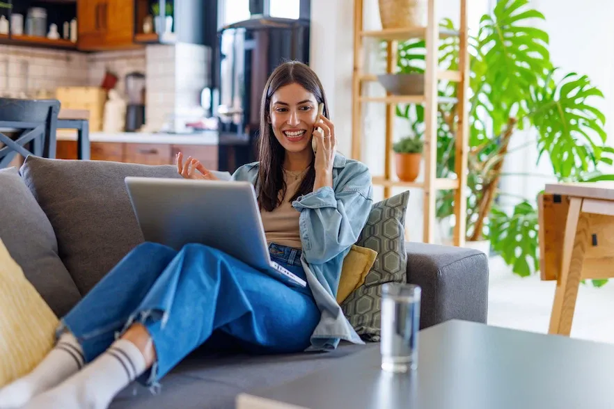 Mujer joven adulta trabajando con una computadora portátil mientras habla por teléfono